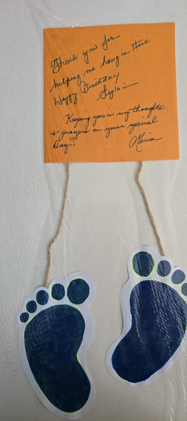 A handmade card of two crayon footprints hanging from a note thanking the practice for helping the writer hang in there.