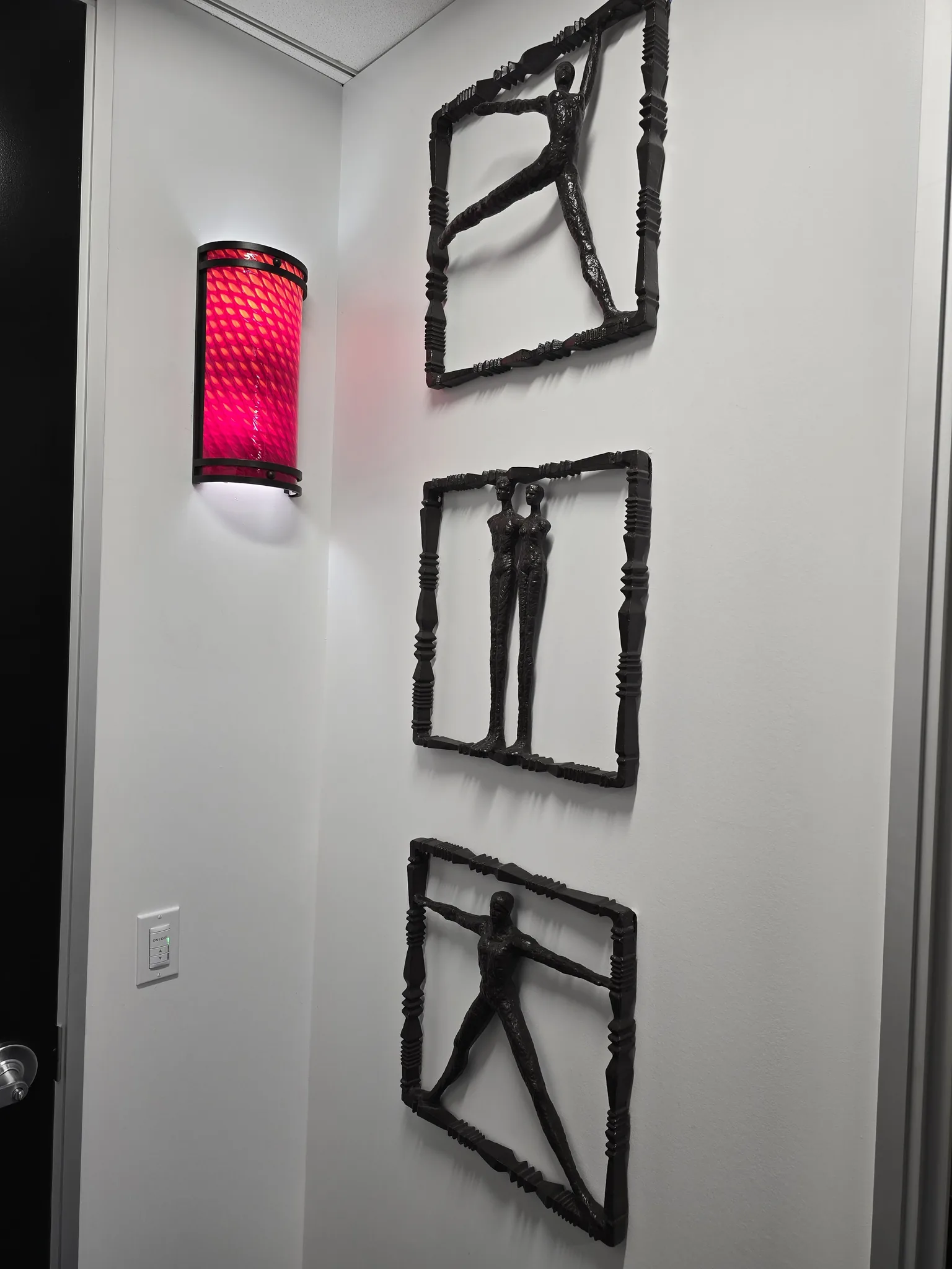 Three sculpted metal figures mounted on a wall beside a red wall sconce