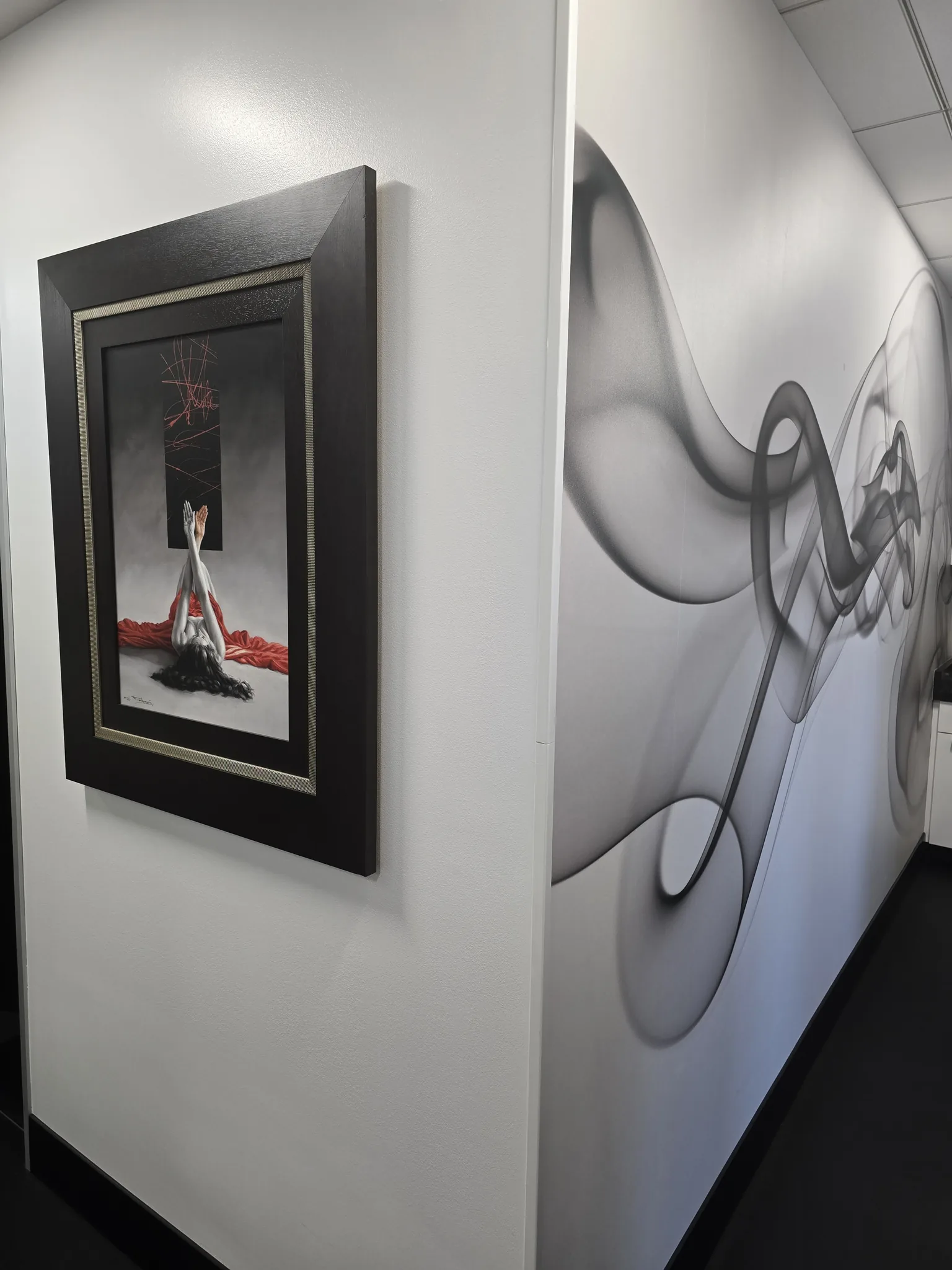 Framed artwork on a white wall beside a flowing grey mural inside Liddy Podiatry