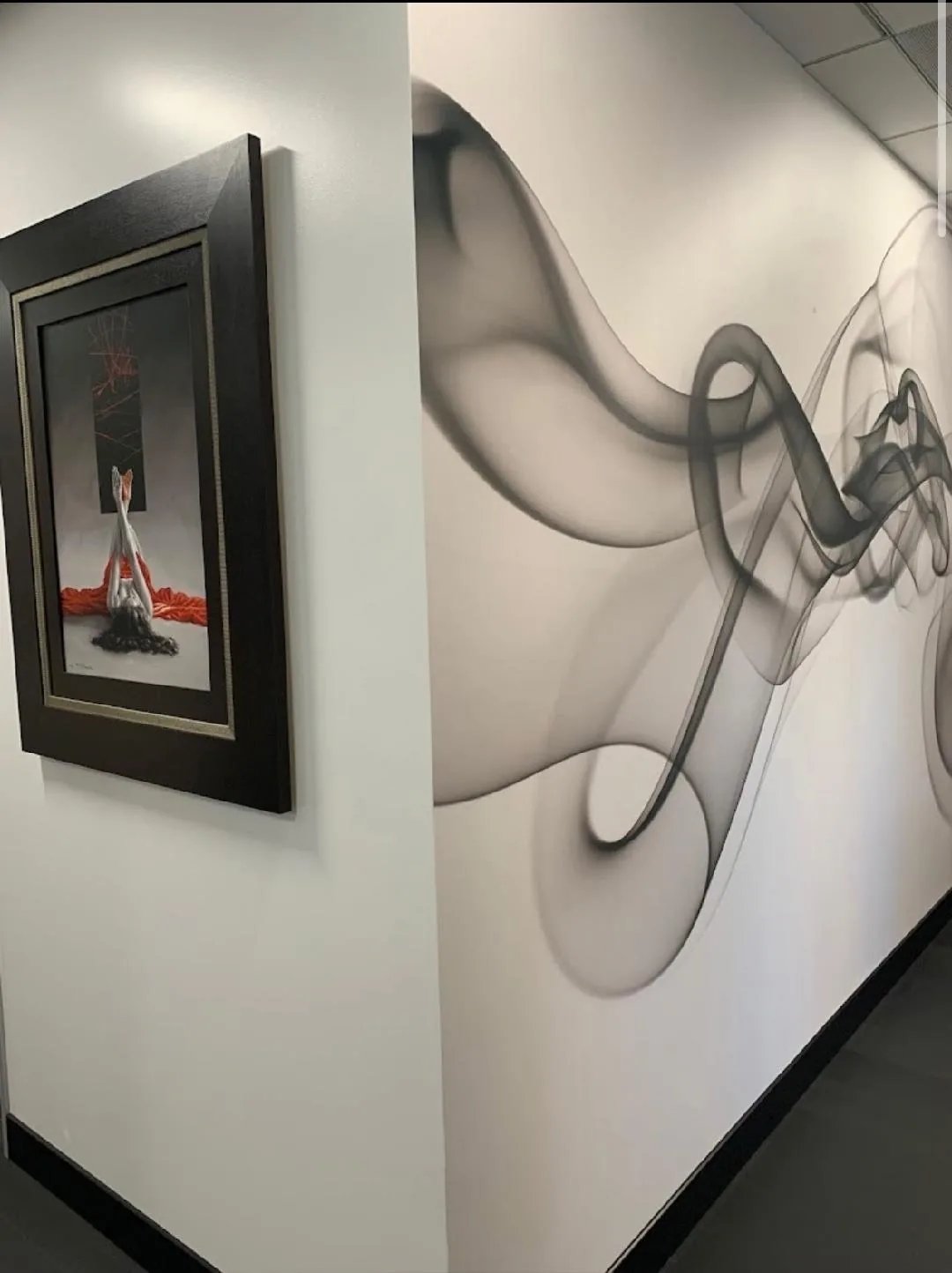 Wider view of the corridor wall with framed artwork and a flowing grey mural