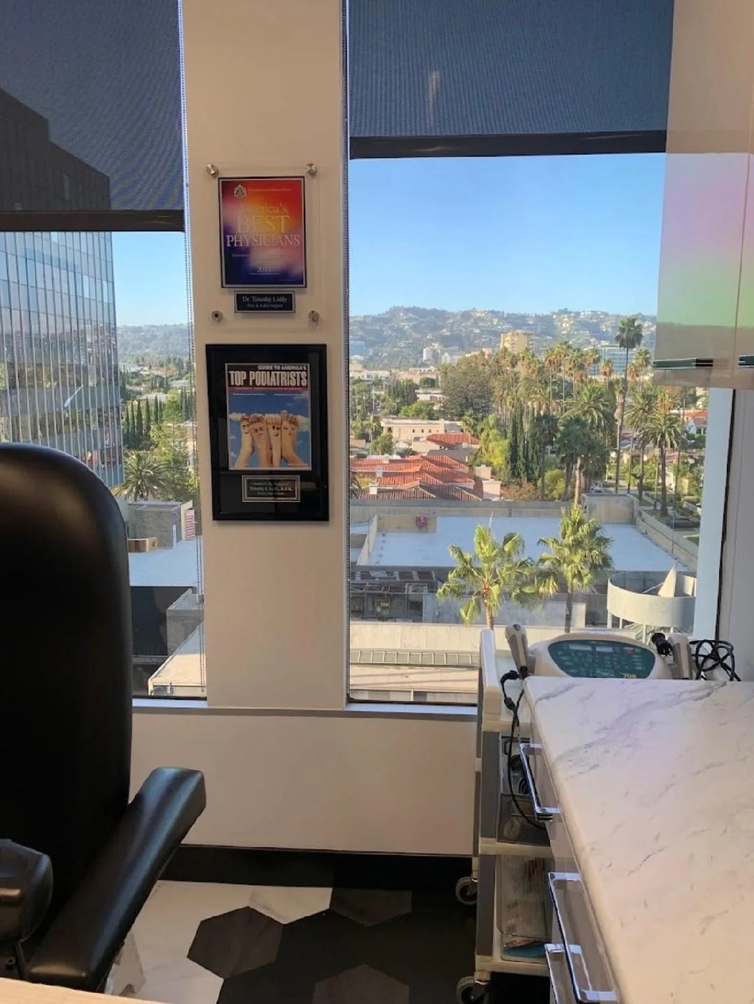 Treatment room with a patient chair, framed awards, and a window overlooking the hills